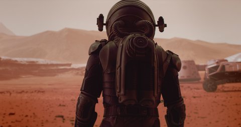 HANDHELD TRACKING back view of astronaut wearing space suit walking on a surface of a red planet. Martian base and rover in the background. Mars colonization concept Video Stok