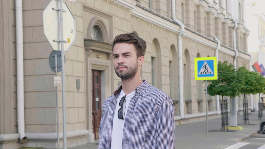 Portrait of handsome stylish hipster lambersexual model. Man dressed in T-shirt. Fashion male posing in the street outdoors. He puts on his sunglasses