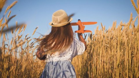 Happy little girl playing with airplane on a wheat field during sunset. Concept big child dream.