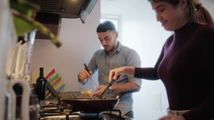 Young couple cooking food together at home with new recipe. Happy man and woman preparing omelette for lunch. Husband and wife smiling in kitchen. Married people and hobby | Shutterstock HD Video #1059188171