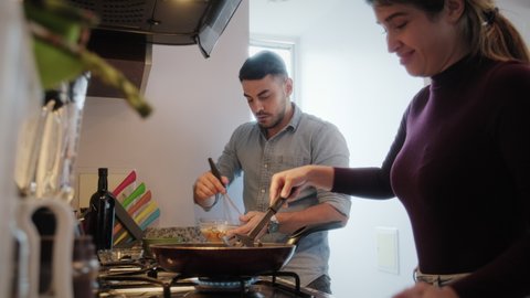 Young couple cooking food together at home with new recipe. Happy man and woman preparing omelette for lunch. Husband and wife smiling in kitchen. Married people and hobby