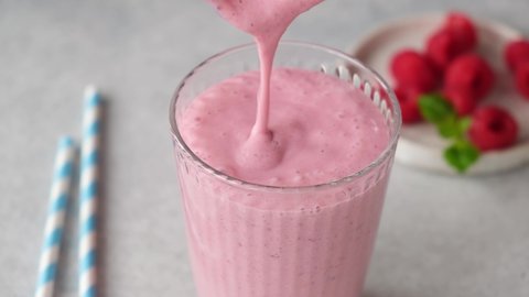 Thick raspberry smoothie pouring in a glass. Healthy refreshing pink berry cocktail