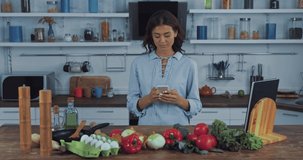 Woman taking selfie with smartphone near fresh vegetables on kitchen table