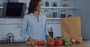 Young woman putting organic vegetables in paper bag on kitchen table