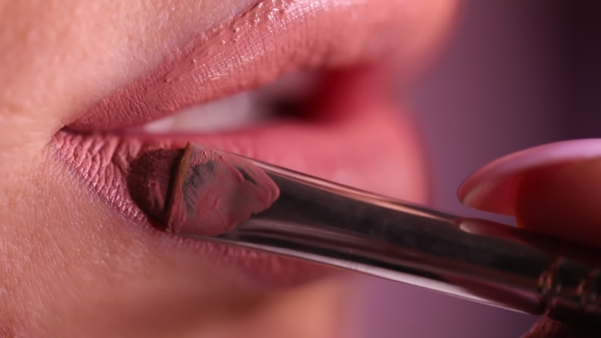 Make up artist applying lipstick. close-up of the lips of a young woman, professional makeup artist with a brush applies natural color lipstick. fashion backstage. beauty saloon. Pink background | Shutterstock HD Video #1059194285