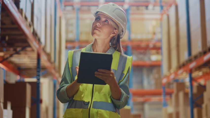 Professional Female Worker Wearing Hard Hat Checks Stock and Inventory with Digital Tablet Computer in the Retail Warehouse full of Shelves with Goods. People Working in Logistics Distribution Center | Shutterstock HD Video #1059197477