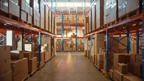 Big Retail Warehouse full of Shelves with Goods in Cardboard Boxes and Packages. Logistics, Sorting and Distribution Facility for Product Delivery. High Moving Backward Between Rows of Shelves Camera