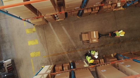 Top-Down Elevating View: Worker Moves Cardboard Boxes using Hand Pallet Truck, Walking between Rows of Shelves with Goods in Retail Warehouse. People Work in Product Distribution Logistics Center