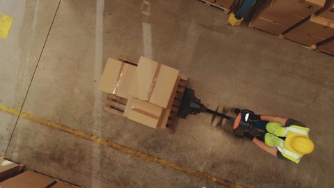 Top-Down Elevating View: Worker Moves Cardboard Boxes using Hand Pallet Truck, Walking between Rows of Shelves with Goods in Retail Warehouse. People Work in Product Distribution Logistics Center