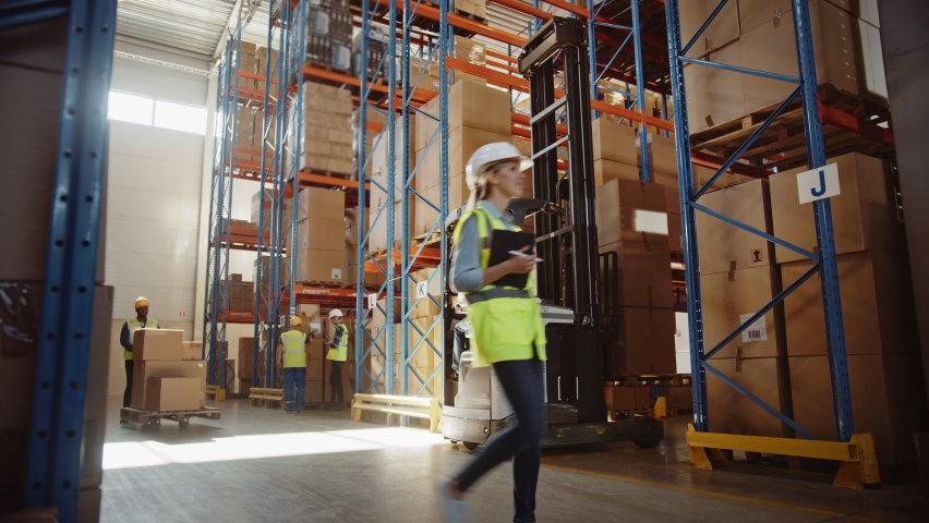 Retail Warehouse full of Shelves with Goods: Electric Forklift Truck Operator Lifts Pallet with Cardboard Box on a Shelf. People Working, Scanning Products, Using Trucks in Logistics Delivery Center Royalty-Free Stock Footage #1059197738