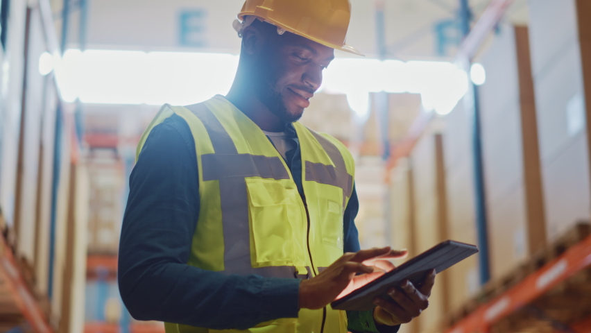 Male Worker Wearing Hard Hat Checks Products Stock and Inventory with Digital Tablet Standing in Retail Warehouse full of Shelves with Goods. Arc Shot with Zoom in on Tablet Computer Royalty-Free Stock Footage #1059197789
