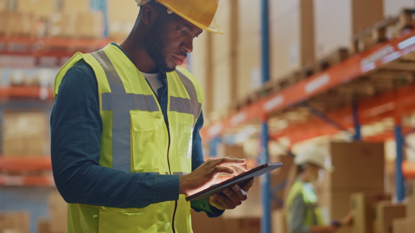 Male Worker Wearing Hard Hat Checks Products Stock and Inventory with Digital Tablet Standing in Retail Warehouse full of Shelves with Goods. Distribution, Logistics. Zoom in on Tablet Computer Royalty-Free Stock Footage #1059197792