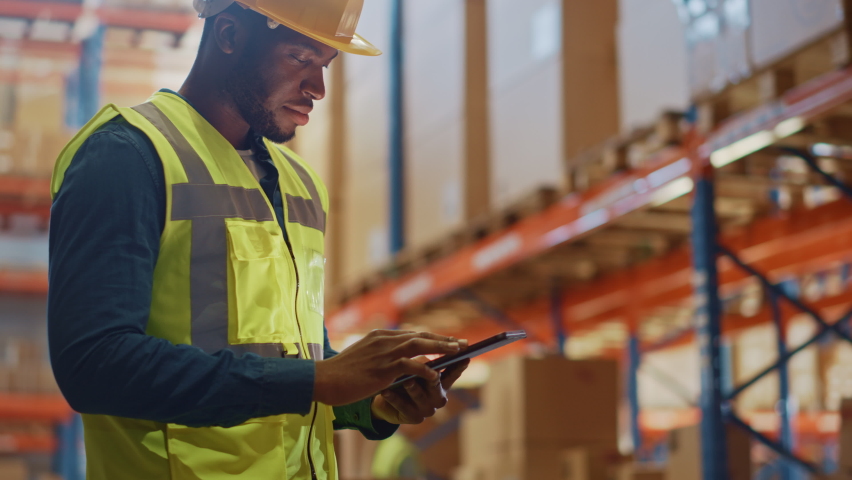 Male Worker Wearing Hard Hat Checks Products Stock and Inventory with Digital Tablet Standing in Retail Warehouse full of Shelves with Goods. Arc Shot Moves to People Operating Forklifts and Trucks Royalty-Free Stock Footage #1059197798