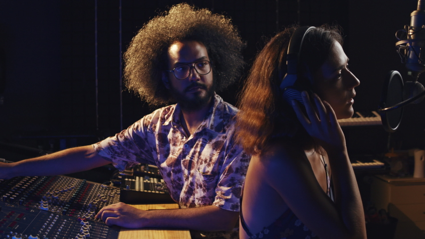 Music studio. Creative people. Hispanic man and woman working in the recording studio. Brunette curly couple is producing songs in comfortable environment. Royalty-Free Stock Footage #1059199217
