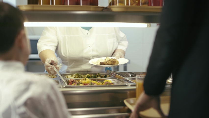 Canteen worker lays a portion stuffed peppers, rice and chicken on the plate in modern school canteen. | Shutterstock HD Video #1059199307