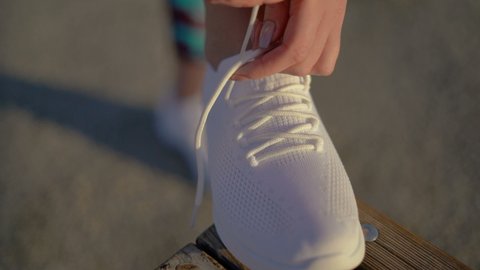 Close-up. women's hands are tying laces on new white sneakers. No logo. The girl put her foot on the bench. 4K