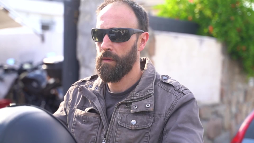 Adult man with beard and sun glasses wears a black helmet looking at the camera