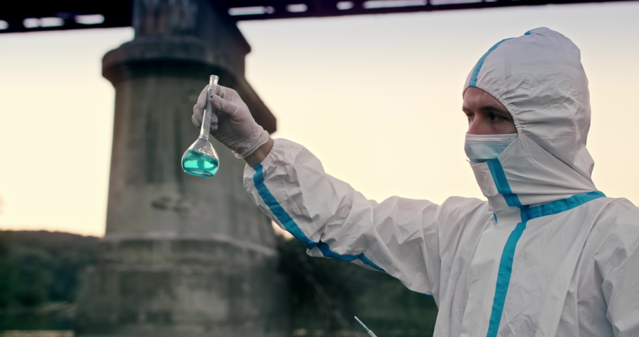 Close up of male chemist ecologist in protective clothing and medical mask taking probes, analysing water samples from dirty polluted river, holding glass tube with chemical agent. | Shutterstock HD Video #1059204446
