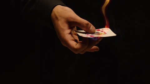 Close-up of a Magician Hand Performing Card Trick . Burning card on black Background with smoke . Card Mechanic rotating flaming ace card in hand . Shot on ARRI Alexa cinema camera in Slow Motion 