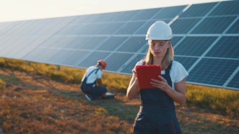 Portrait of smart lady engineer using electronic tablet monitoring solar panels and smiling happy. Teamwork. Sustainable energy. Solar power field. Ecology.