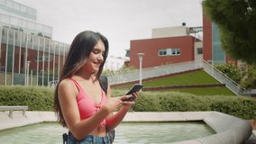 Happy young latin woman talking and texting on smart phone, wearing casual clothes sitting on bench. Generation z students life, girl online shopping near campus, social media and video conference.