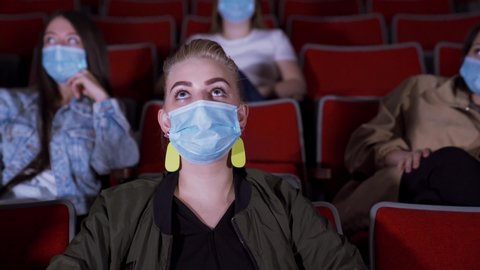 People in masks watch funny movie. Media. People in medical masks sit in movie theater and laugh while watching movie. Opening of cinemas during pandemic coronavirus