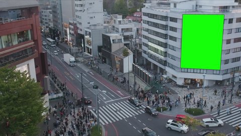 Large billboard with a green screen for advertising, on the modern building, busy crossroad with neon lights, traffic, crowd, Tokyo, Japan. 