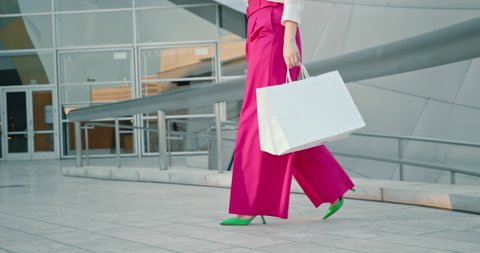 Fashion shoes. Slow motion 4K fashionable green heels and hot pink trousers. Stylish blogger in pumps walking outside business center. Woman in pink outfit with white shopping bags on urban background