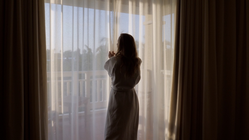 Beautiful woman opening curtains and walking outside on the balcony. Woman in hotel room opens curtains and walks outside, beautiful garden view Royalty-Free Stock Footage #1059228776