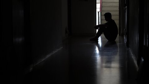 Silhouette of a stressed man sitting in the dark leaning against the wall in old condo, Stress, violence, The concept of depression and suicide.