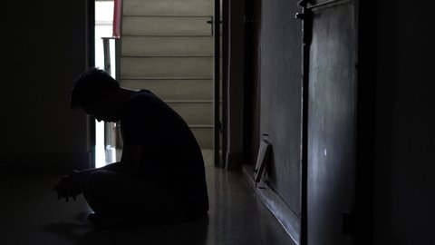 Silhouette of a stressed man sitting in the dark leaning against on steps in old condo, lost in life, violence, The concept of depression and suicide.