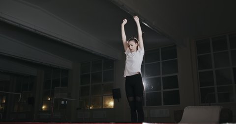 Girl gymnast jumps on trampoline in the hall. Stain, made professionally in a dark gym with single bright spotlight.