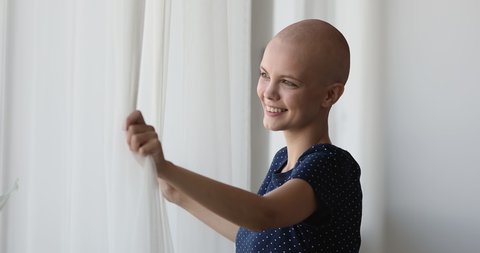 Cancer patient happy bald woman standing near the window looks outside breath fresh air feels alive enjoy new day. Remission, oncology recovery, finally victory over disease, effective therapy concept
