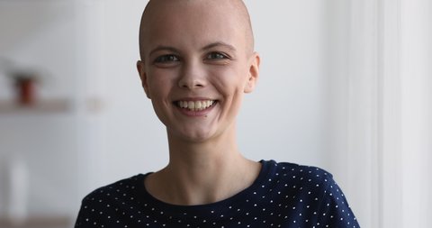 Close up view bald 20s woman standing indoor smile look at camera. Portrait of hairless cancer patient fighter. Remission and recovery, rehabilitation and new day of oncology disease person concept