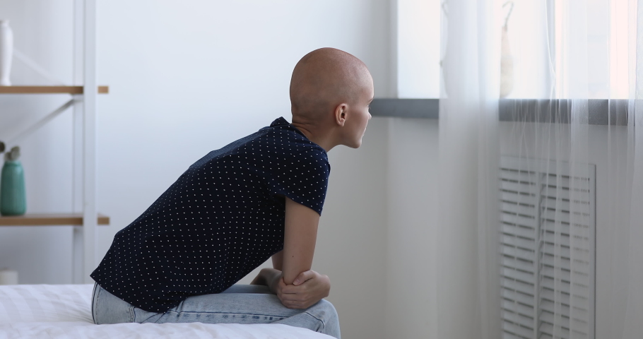 Young bald woman cancer patient sitting on bed in hospital ward alone looking out the window thinking about oncology disease feel abandoned and unhappy. Battling with tumor, recovery in clinic concept | Shutterstock HD Video #1059236138