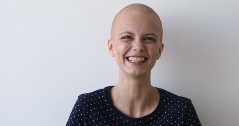 Bald hilarious young woman breast cancer patient posing on grey wall background laughs feels carefree believes in recovery celebrates remission, overcome oncology disease head shot studio portrait