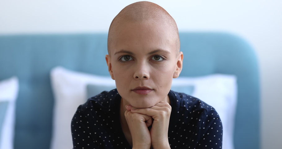 Close up head shot portrait young pretty bald woman sit on bed in bedroom put chin on hands smiling looking at camera feels happy. Successful fight against cancer disease, belief in recovery concept Royalty-Free Stock Footage #1059236198