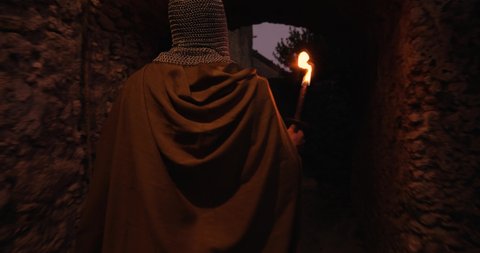 Viking or Norman man with a flaming torch, walks between the walls and streets of his city in the night.