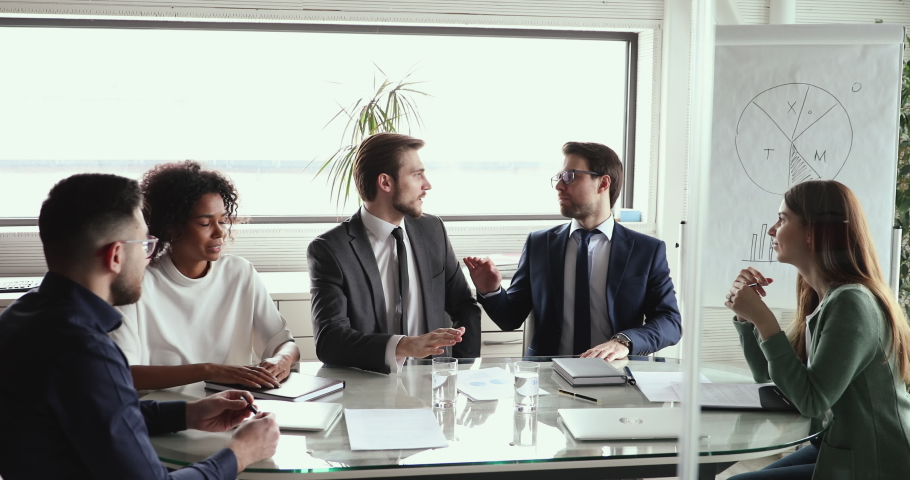Interested multiethnic business people listening to two partners briefing conversation, sitting together at table in modern work space. Motivated executive managers discussing development strategy. | Shutterstock HD Video #1059240578