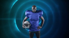Digital composite video of Male rugby player holding helmet against blue glowing circles on black background. Sports fitness concept digital composite