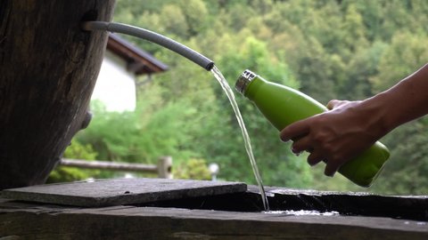 Italy , Alps Devero Piedmont - Mountain wooden fountain - hand filling up a green water bottle cooling  with spring water in nature landscape 