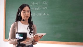 Portrait of smiling Asian female teacher in headset working in classroom teaching online explaining math in blackboard to student study from home.Distant education,during quarantine,COVID-19 epidemic.