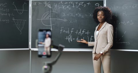 Smartphone recording video lesson at school. Online studying. African American young female teacher explaining math or physics formulas at class. Quarantine concept. Study by internet. Isolation.