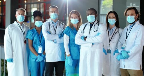 Multi ethnic women and men, doctors. International medics in medical masks. Protected healthcare workers. Mixed-races physicians and nurses looking at camera. Clinic team. Docs at work in hospital.
