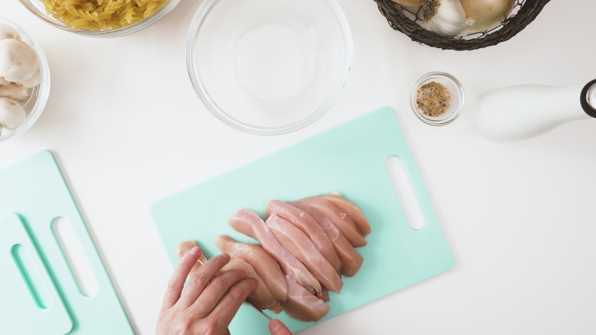 Woman chopping fresh raw chicken breast meat close up on cutting board, view from above, white kitchen table background Royalty-Free Stock Footage #1059253793