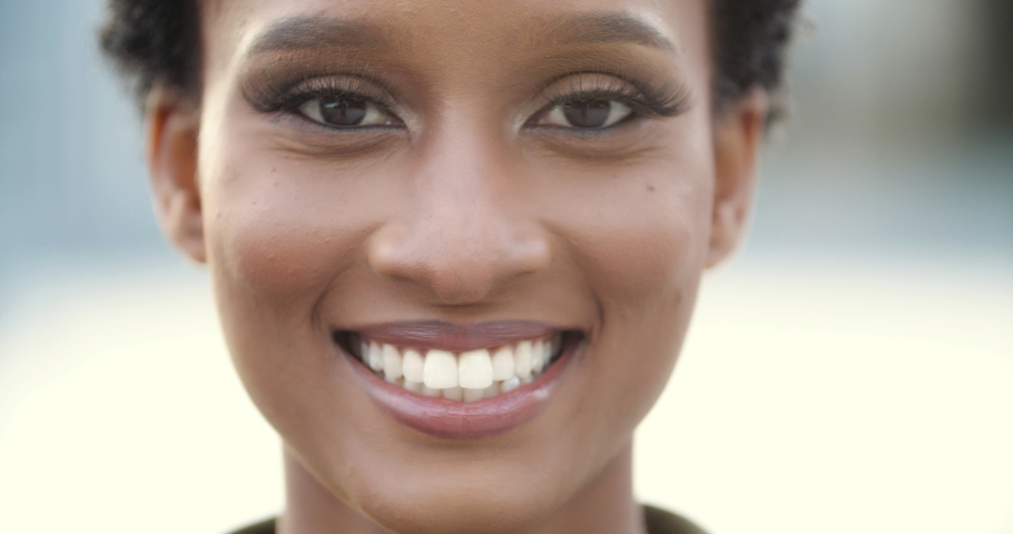 Front close up of mixed race woman, beautiful young human face with black skin, serious look at camera open and confident. Girl wide smiling with healthy white teeth. Portrait of African American lady