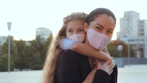 Woman in medical mask, mother holds child in hands on back on street walk in coronavirus epidemic, look lovingly at camera, supports protects baby. Mom hugs daughter in pandemic respiratory virus risk