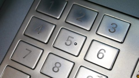 A woman's hand dials the code on the ATM metal keyboard close up