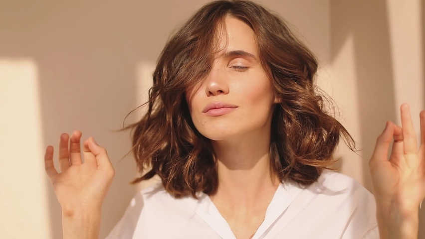 Cheerful young woman enjoying good smell or pleasant fragrance, feel calm breathe fresh air managing stress practicing exercises, wears white shirt, peaceful woman. Short curly brunette with woman. | Shutterstock HD Video #1059261056