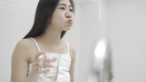 A cute Asian woman brushing her teeth and gargling in front of the mirror after waking up every morning.